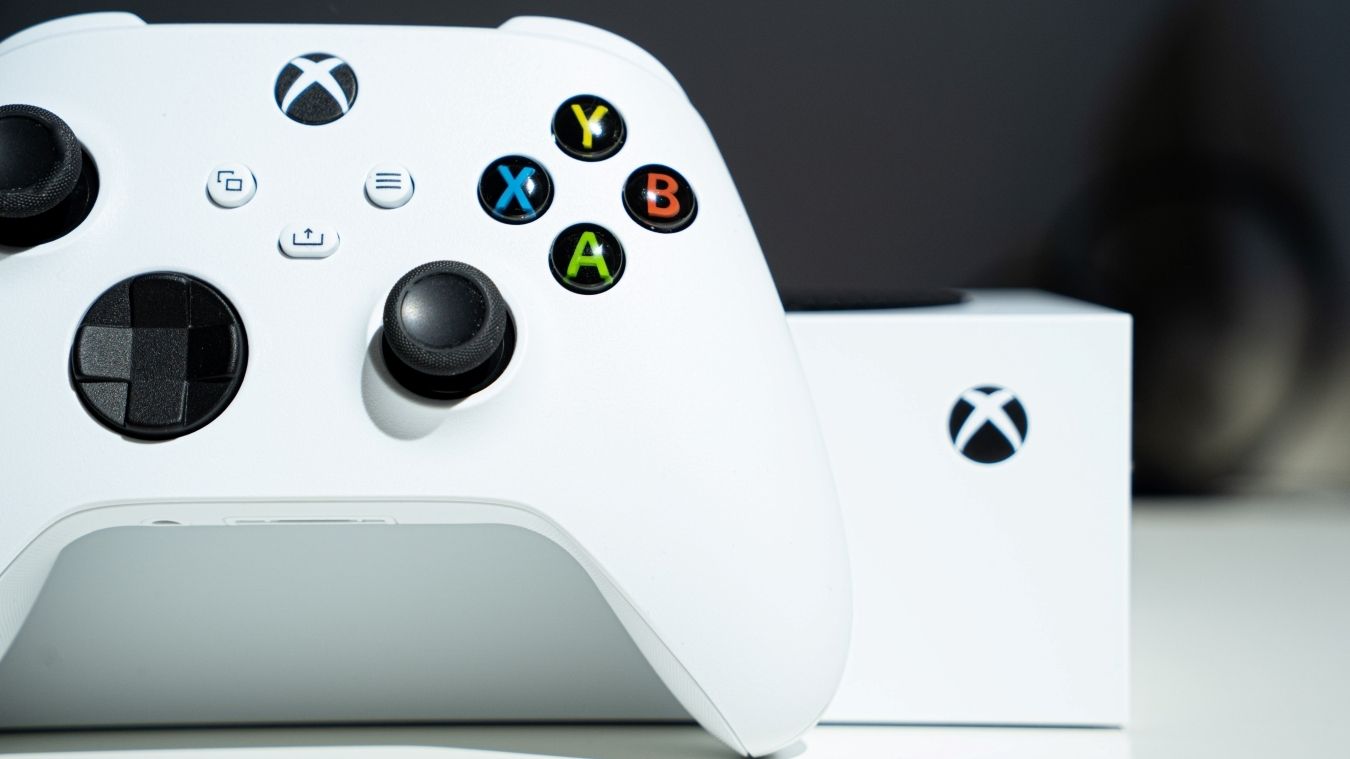 A photograph of an Xbox Wireless Controller resting against an Xbox Series S 