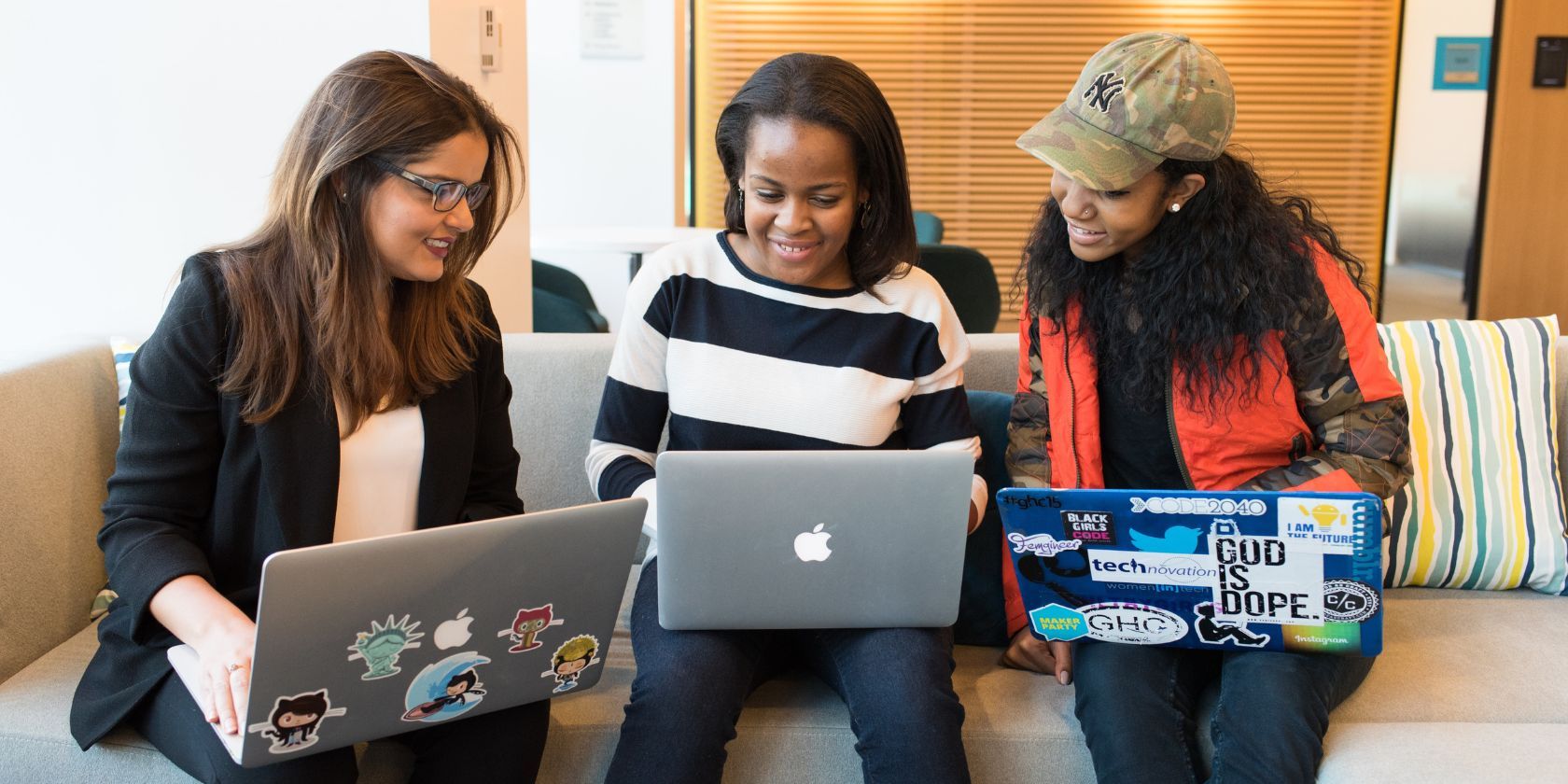 three women smiling with open laptops on their laps