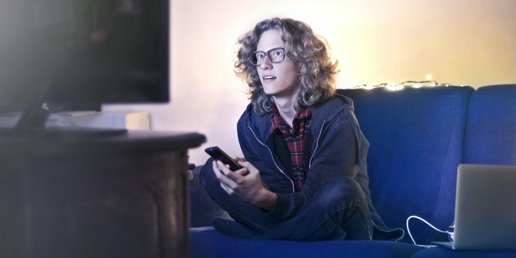A young man watching TV and sitting beside a MacBook