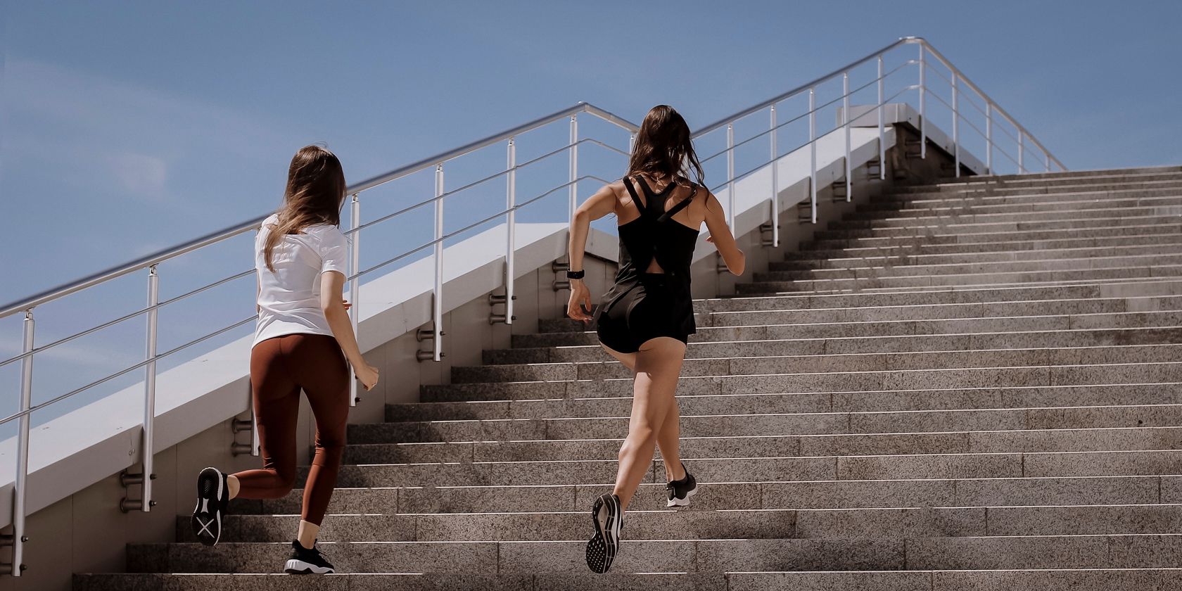 Two women running up grey concrete stairs