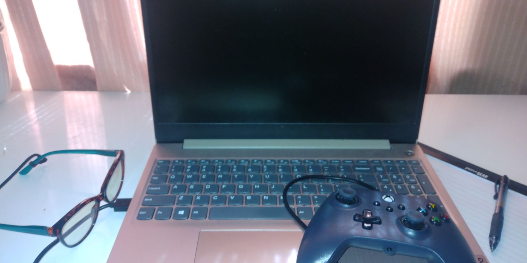 blue-light glasses, controller, notepad, and laptop on a desk