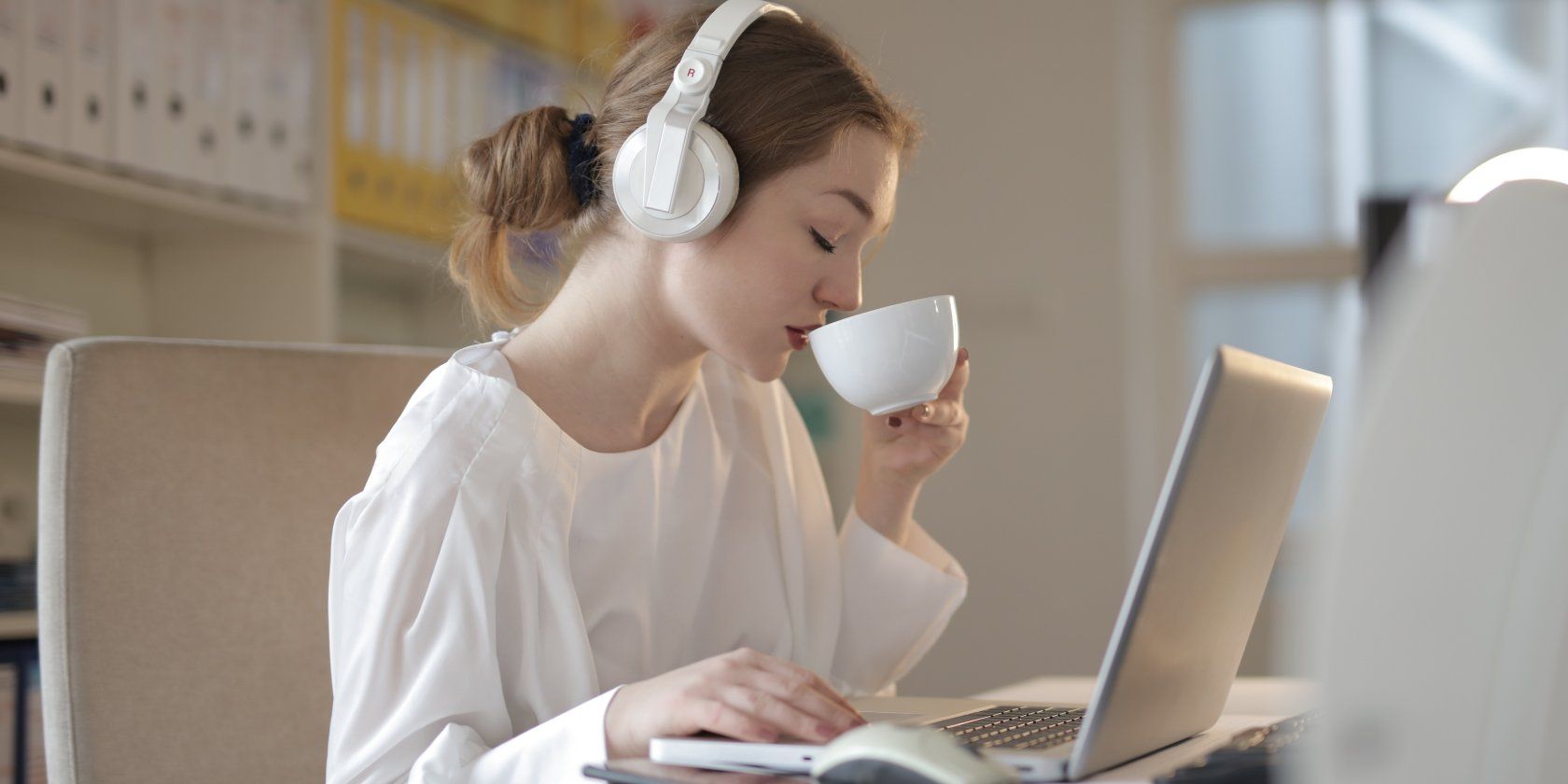 Woman drinking coffee listening to music in front of computer