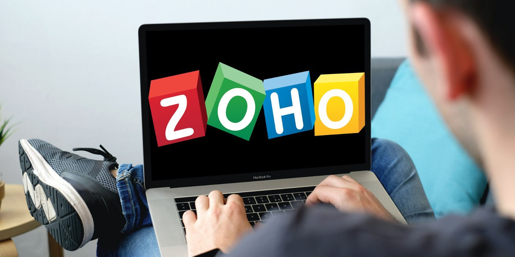 Zoho logo on laptop screen placed on a lap of man. 