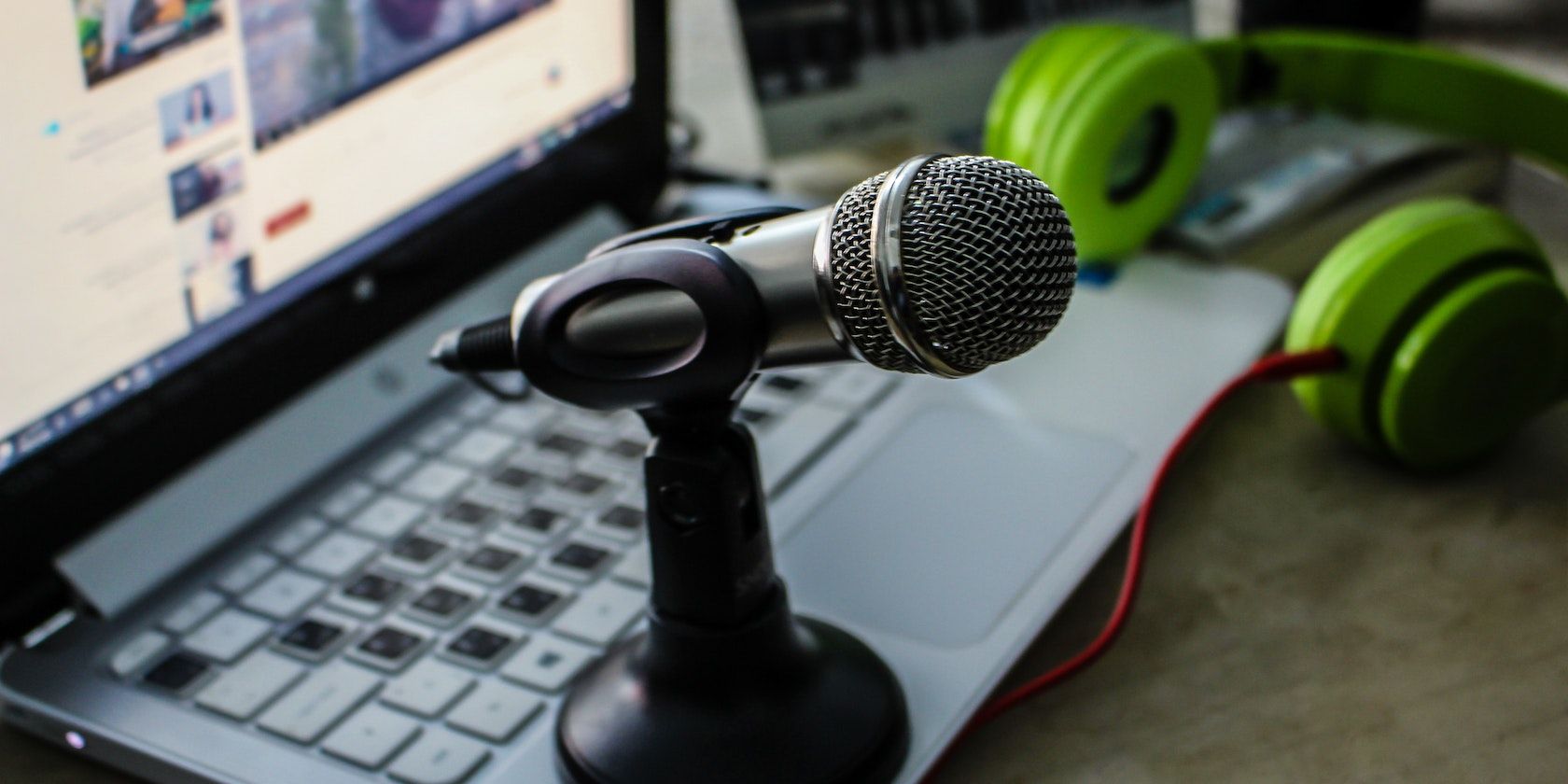A black microphone on a laptop with green headphones in the background