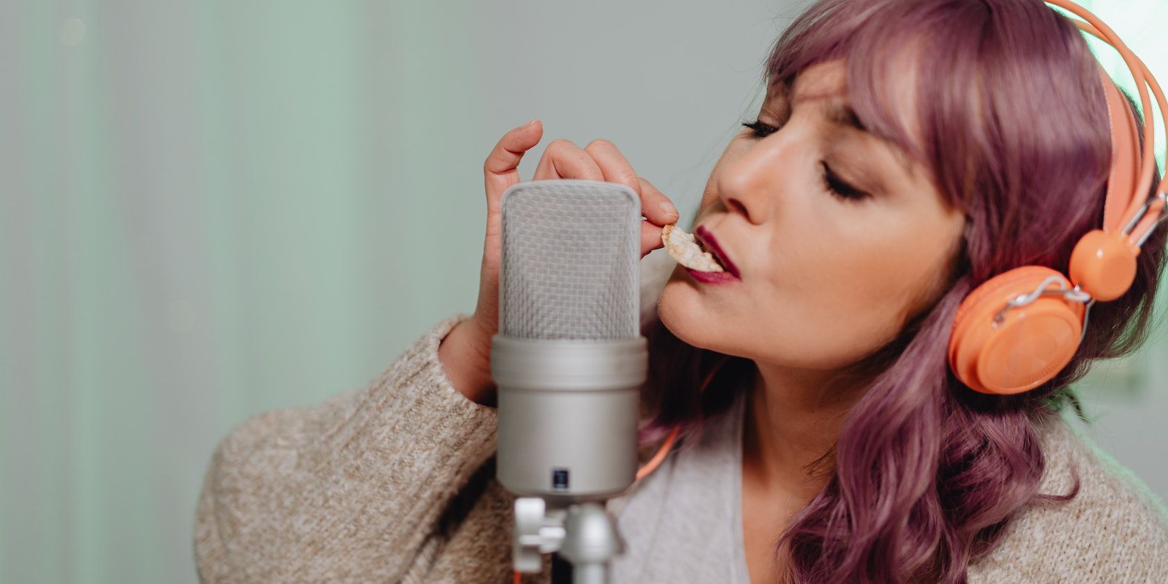 A woman in gray sweater eating a biscuit near a microphone