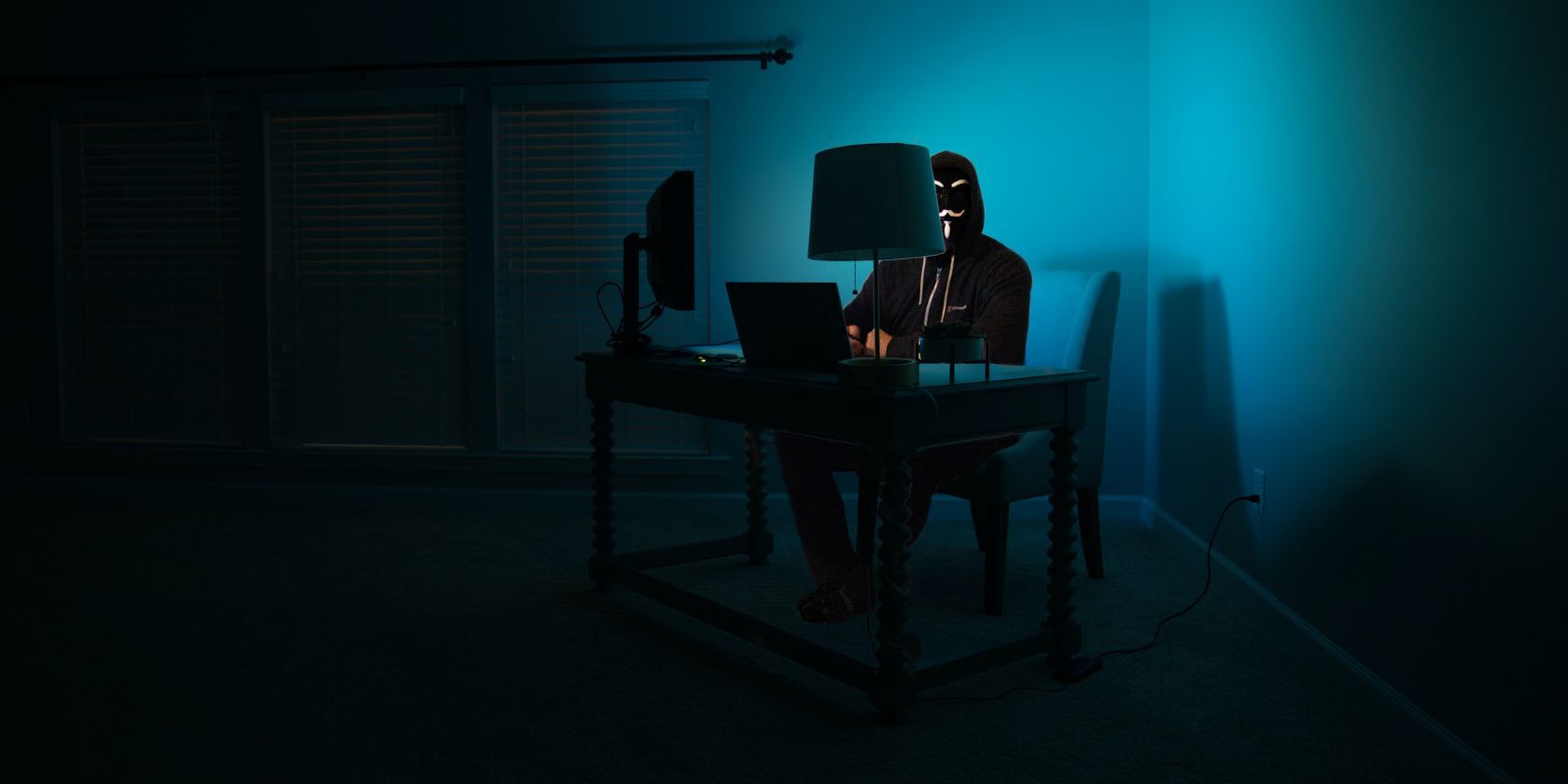 cá nhân đeo mặt nạ ngồi trước máy tính trong phòng tối 
