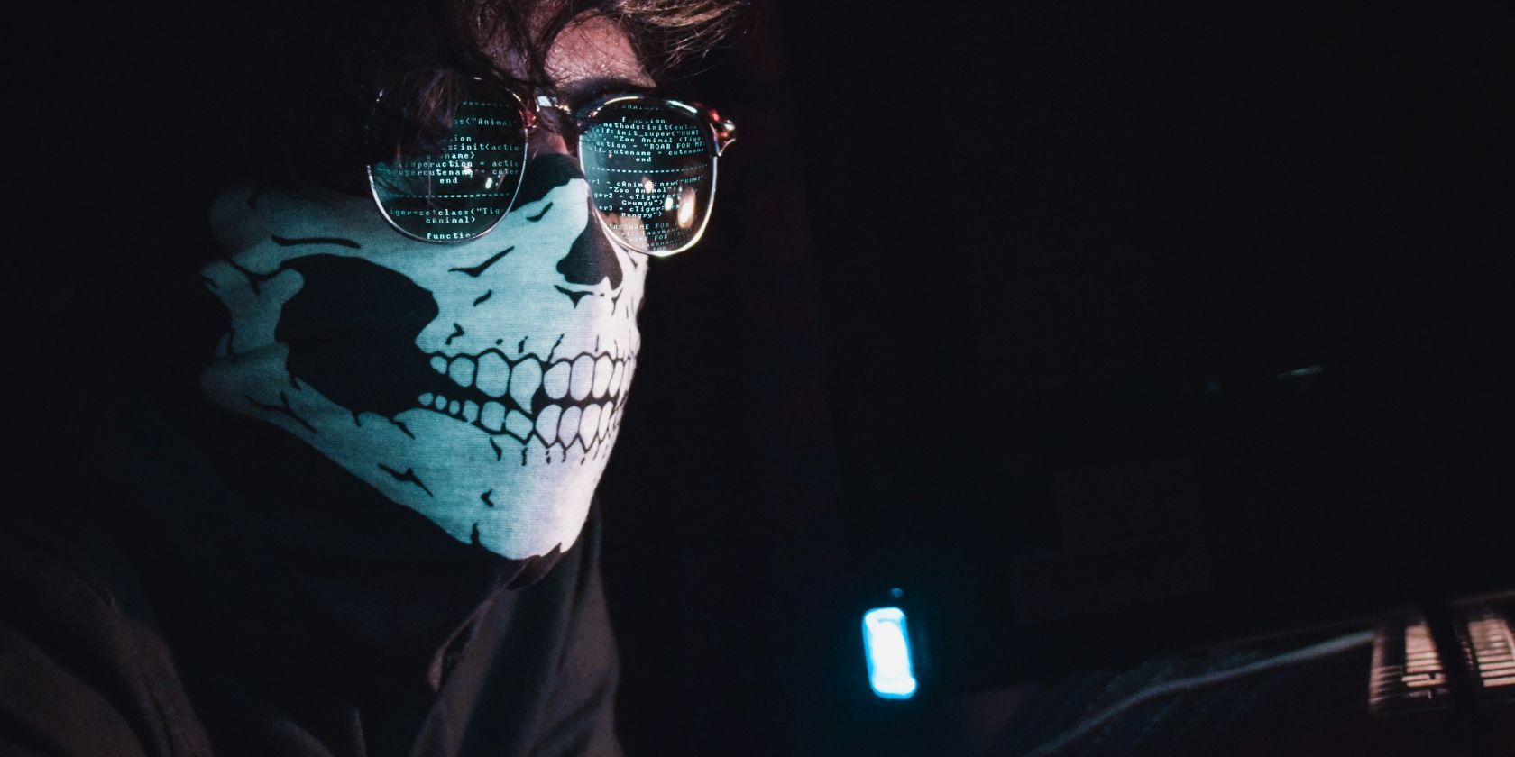 hacker wearing sunglasses and skull mask at computer desk