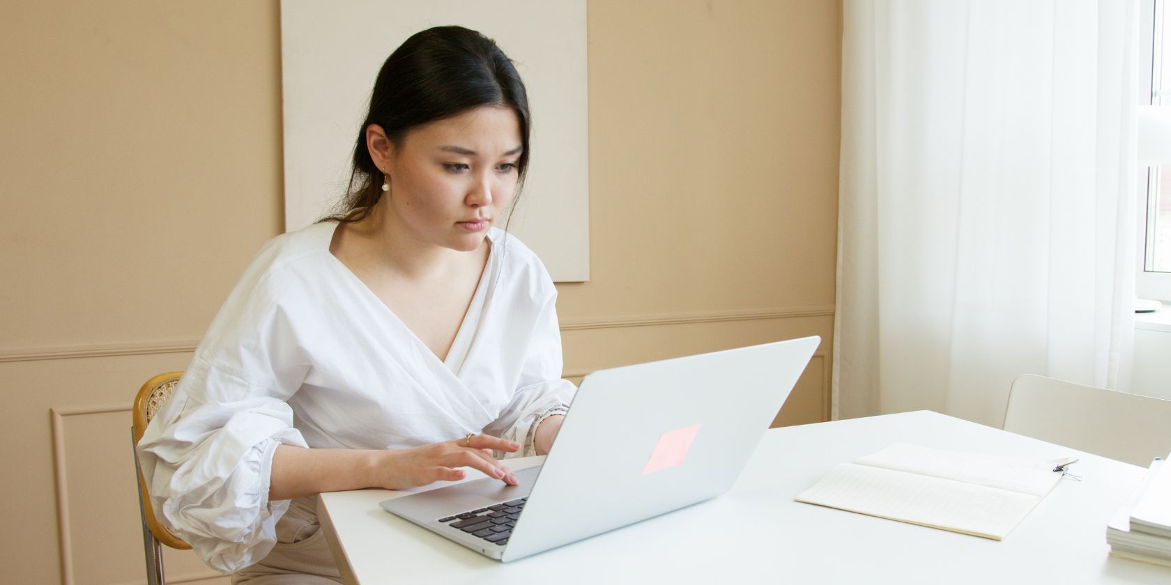 woman wearing a white blouse typing intently on laptop