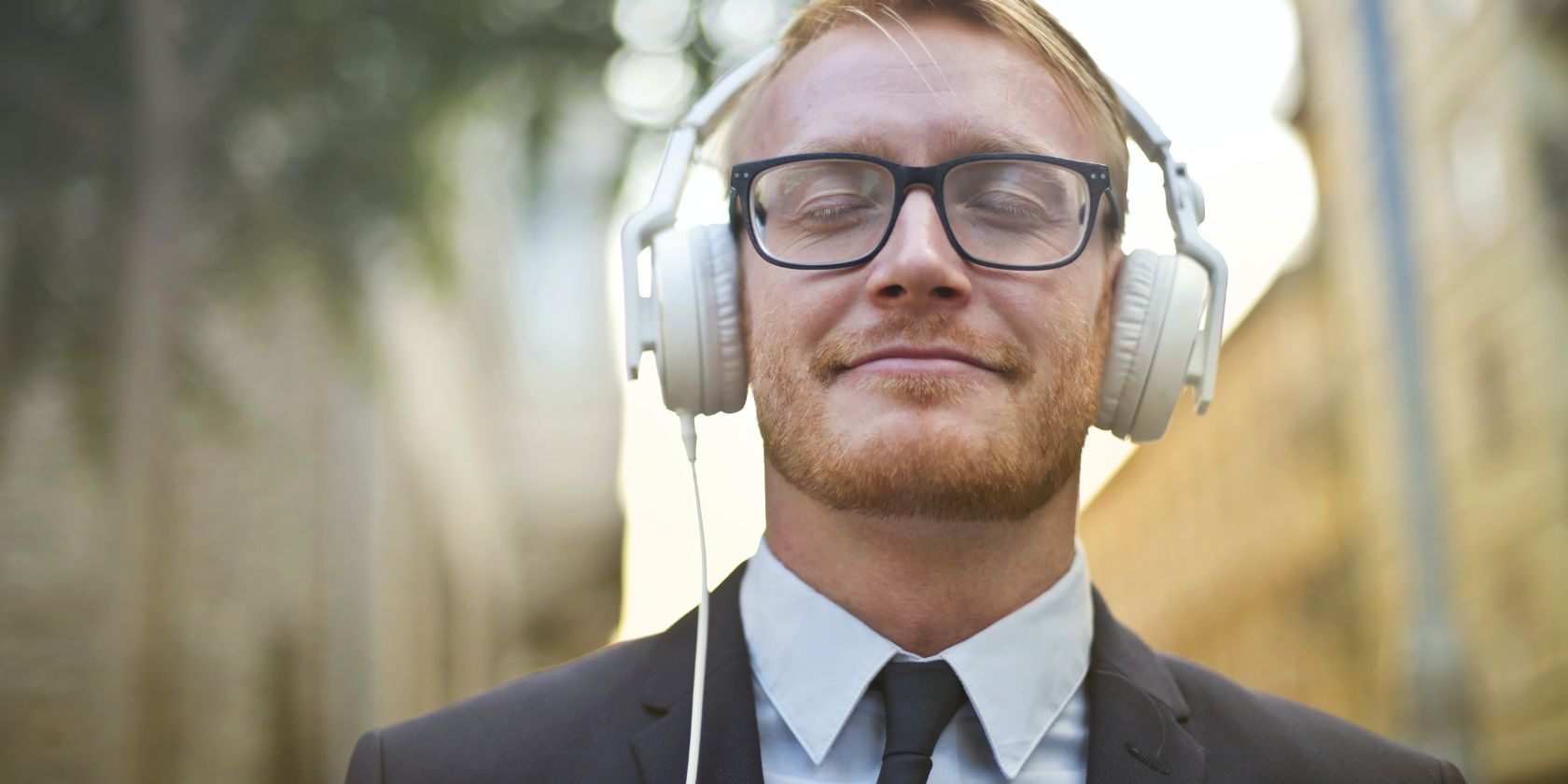 Smiling man enjoying music on his headphones and wearing a business suit
