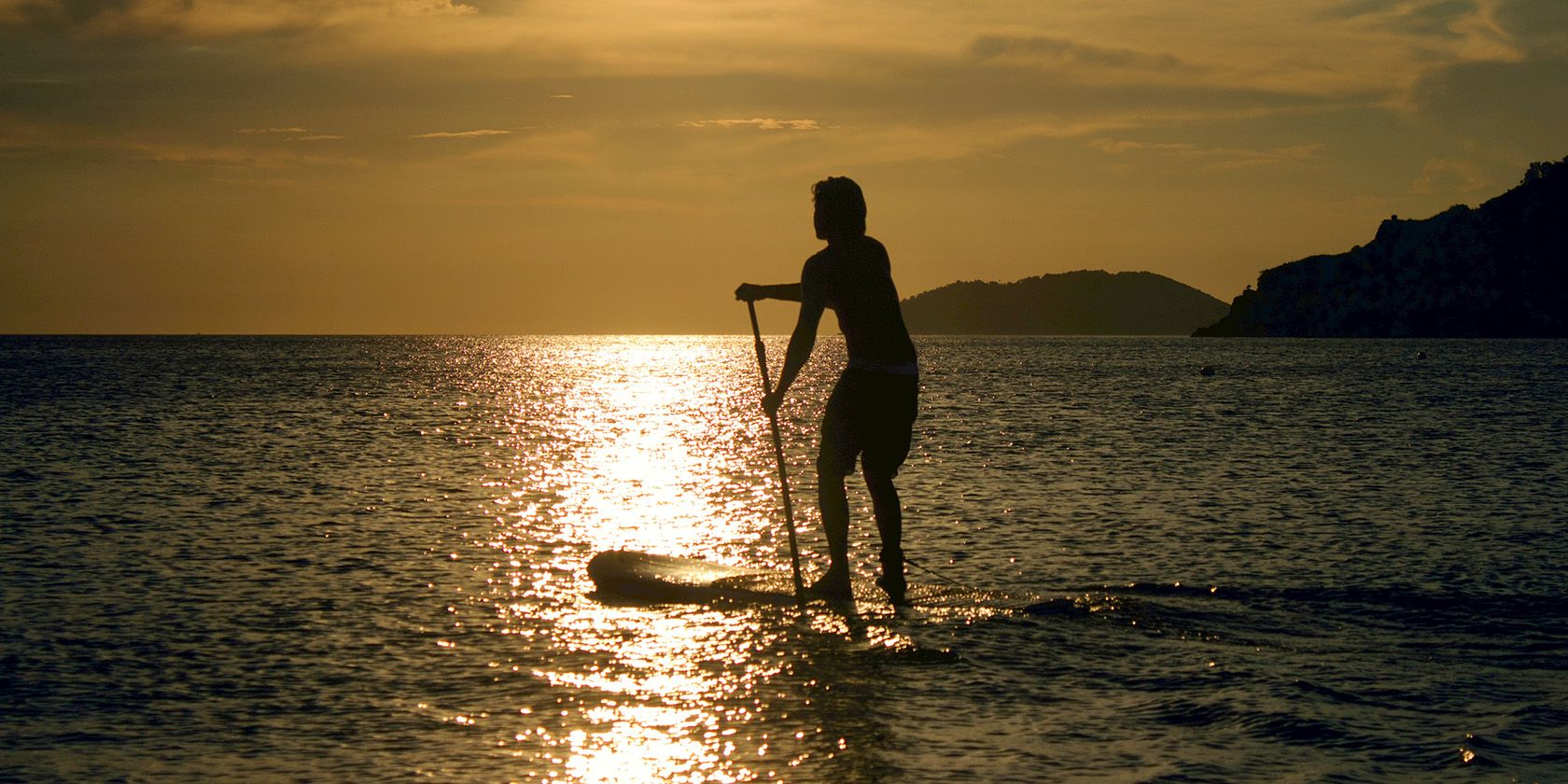 Person paddleboarding at sunset