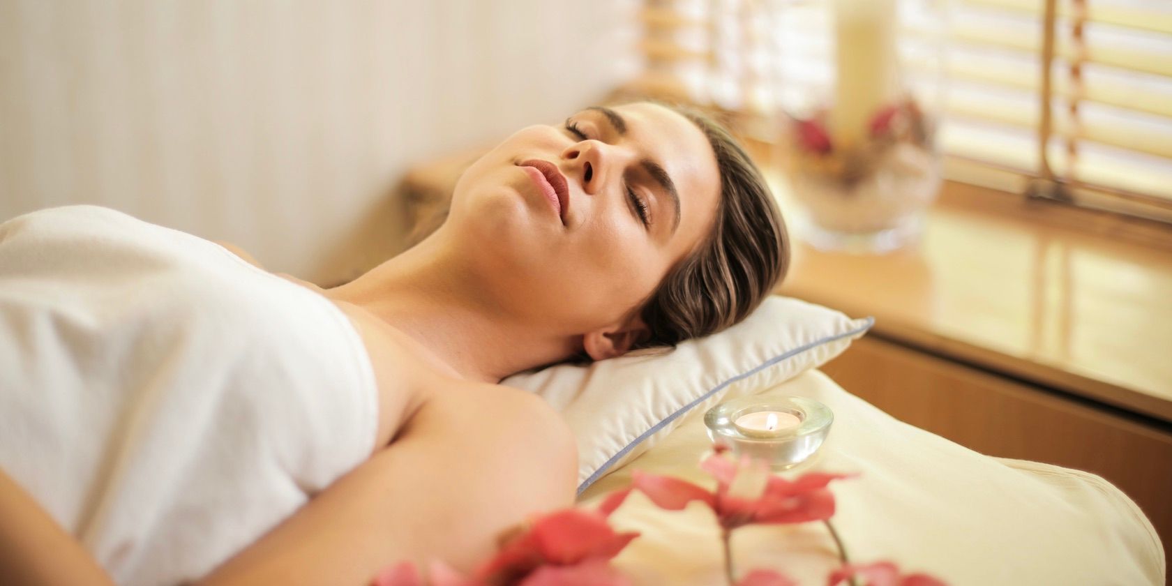person lying in white towel at spa with eyes closed