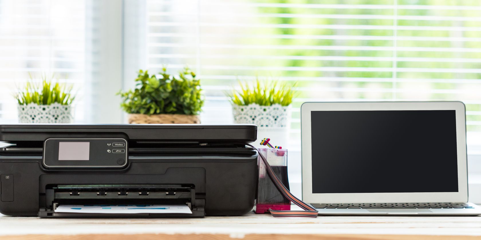 Black printer on desk next to MacBook Air laptop