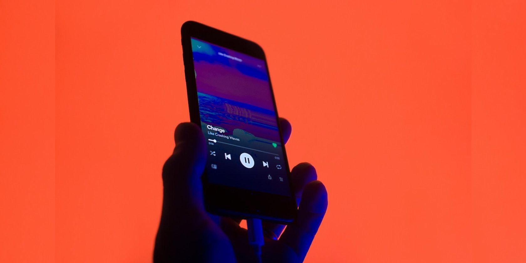 A hand holding a phone displaying a song on Spotify 