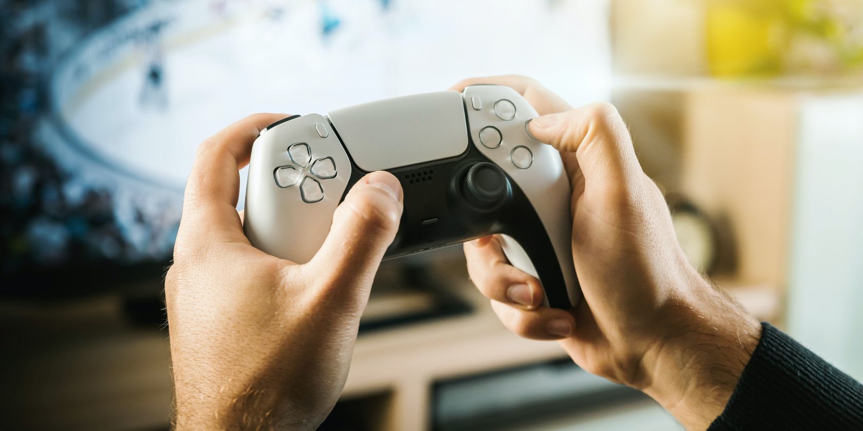 Two hands gripping a PS5 controller with a TV in the background