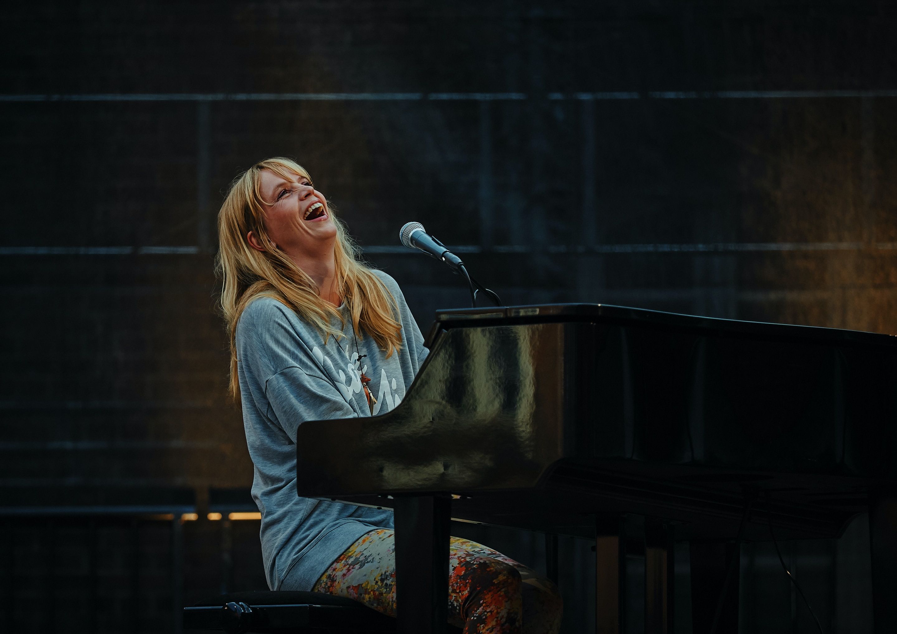 Người phụ nữ mặc áo sơ mi xanh chơi piano và cười