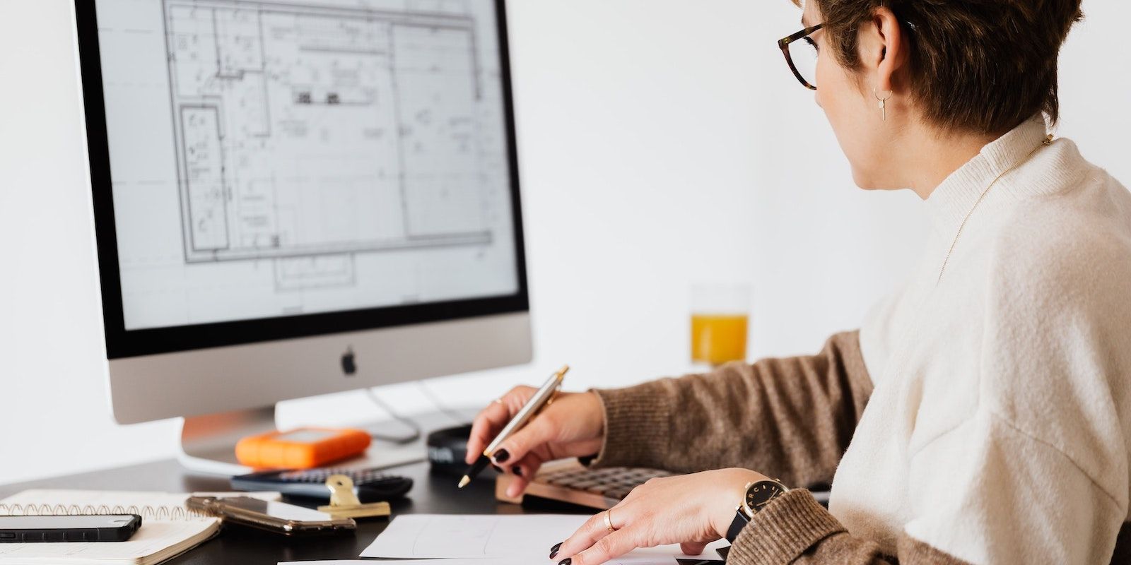 Người phụ nữ đeo kính viết trên máy tính xách tay trong khi sử dụng iMac