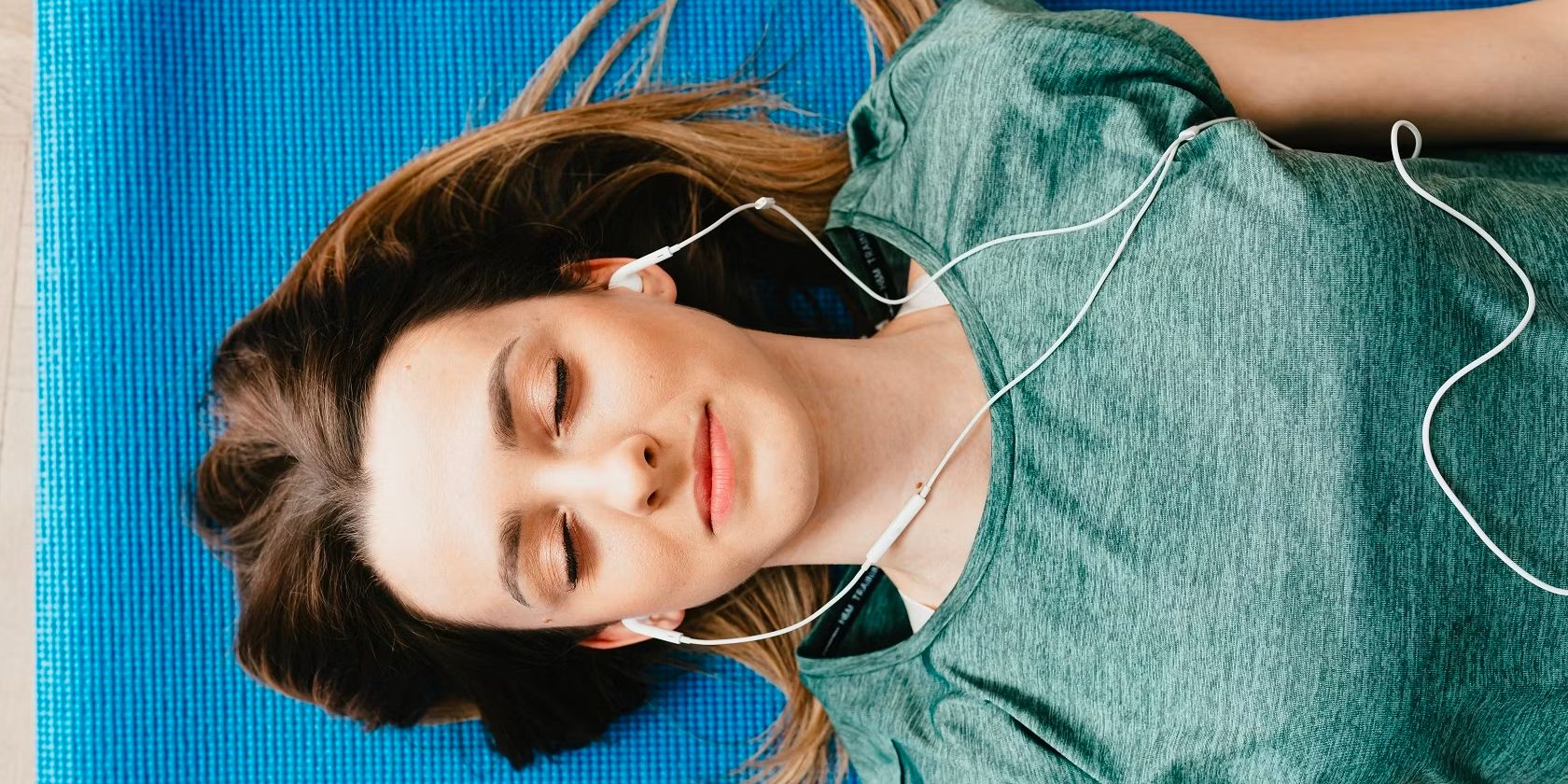 Woman resting on yoga mat wearing earphones