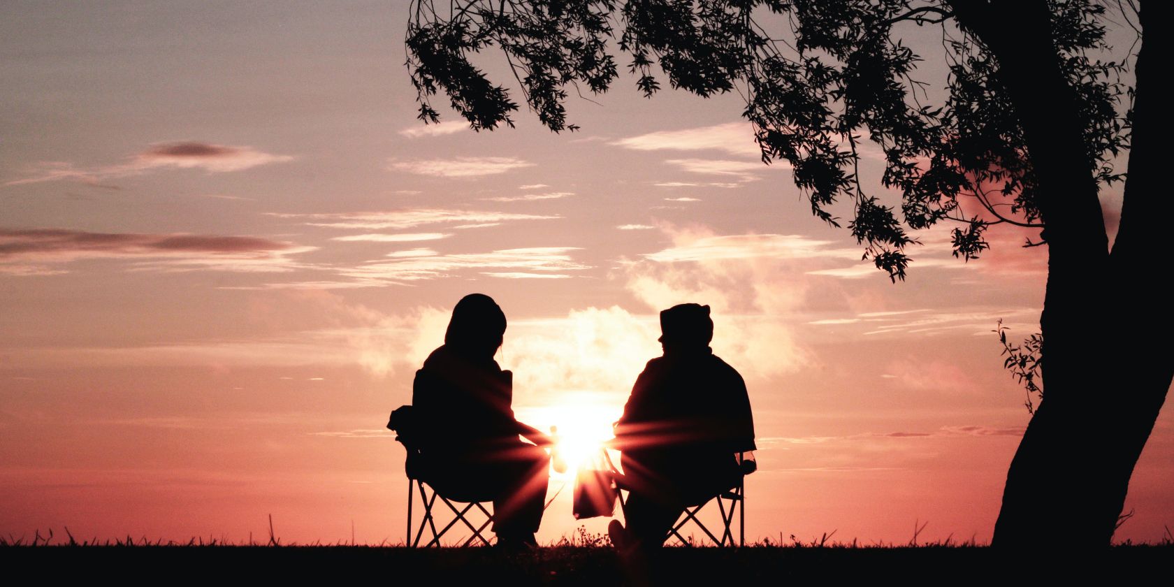A couple sitting on chairs in front of sunset