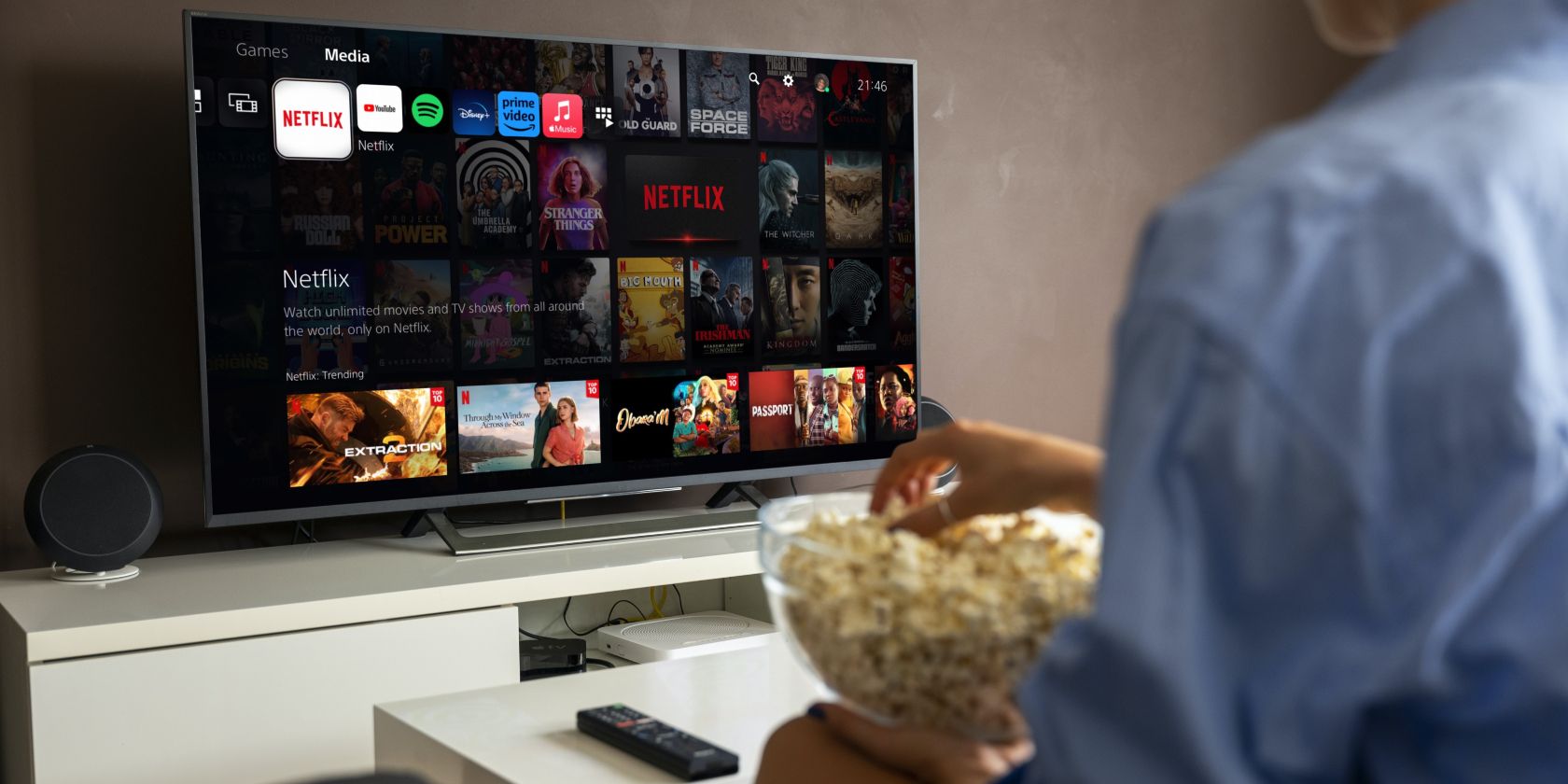 A woman with popcorn sitting at a smart TV with PS5 Netflix on the screen