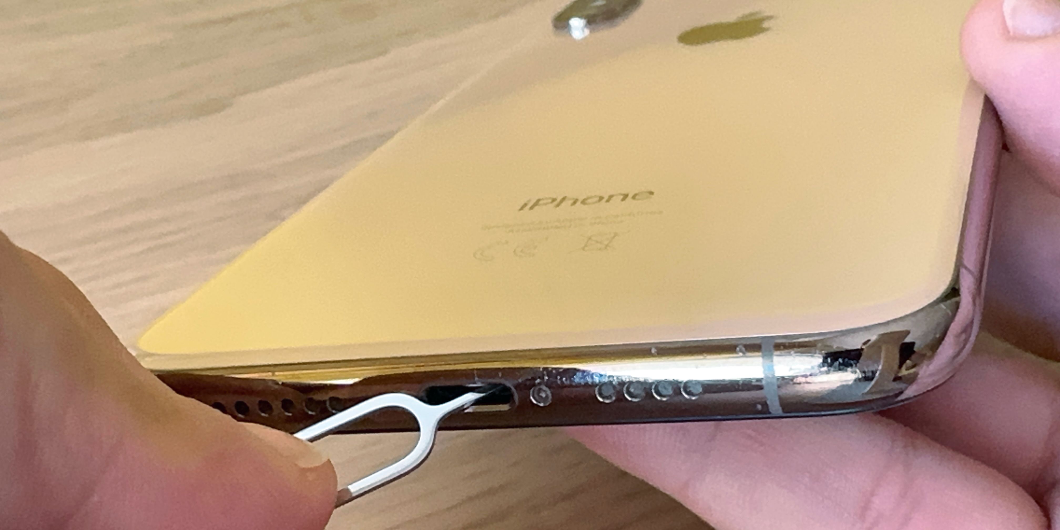 iPhone XS Max in hand, with a SIM Card Eject tool inserted in the Lightning port