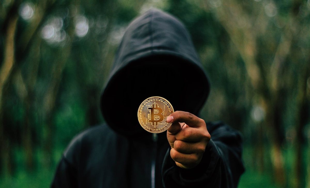 A person with a hoodie holding a golden Bitcoin