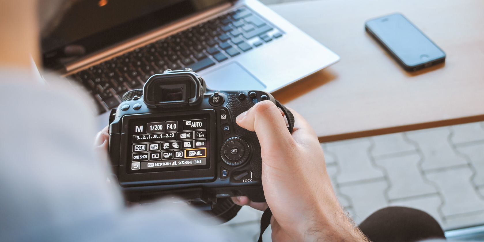 Person holding black DSLR camera with photo settings open