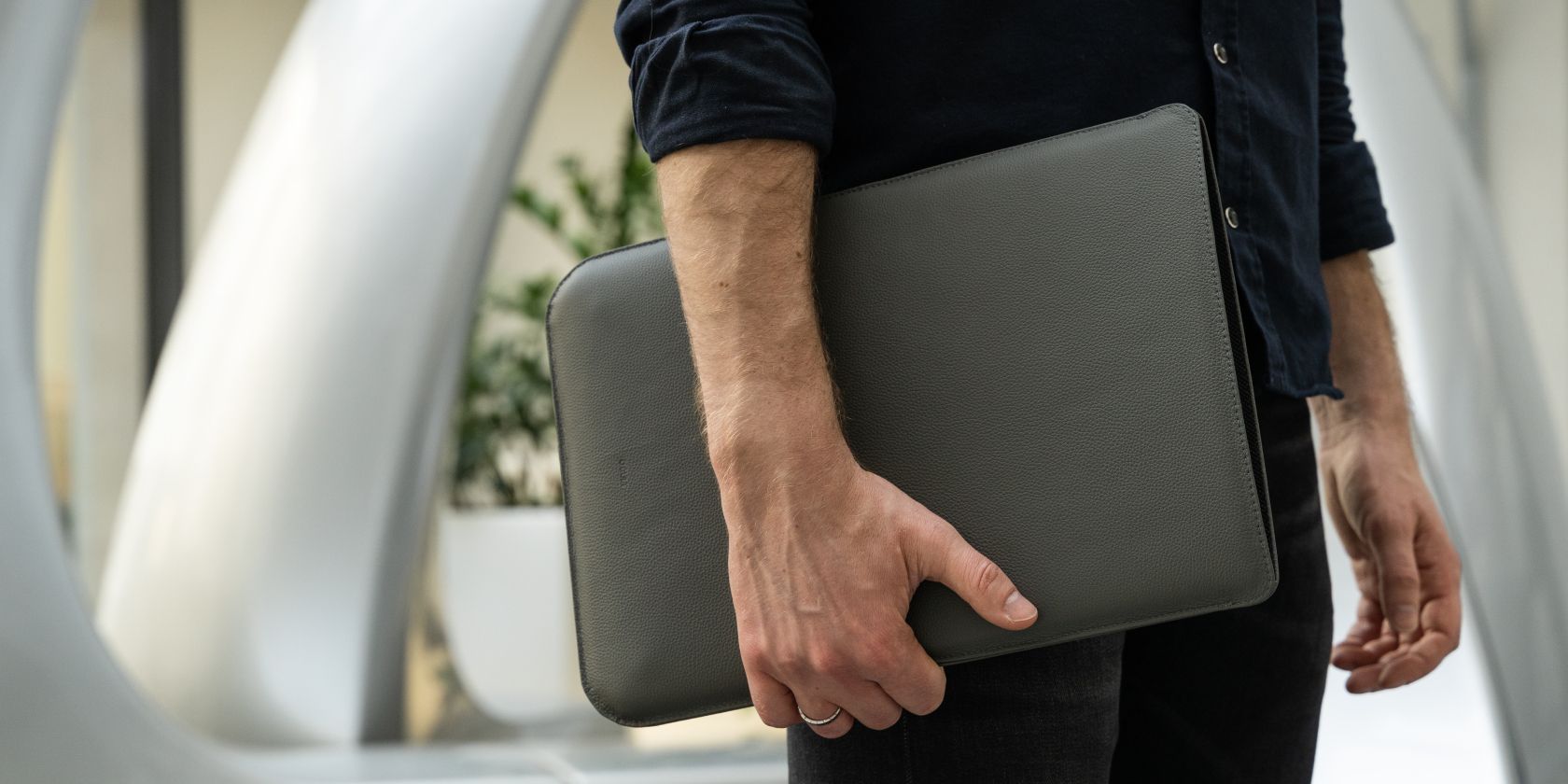 Peron holding a laptop in a leather sleeve at waist level