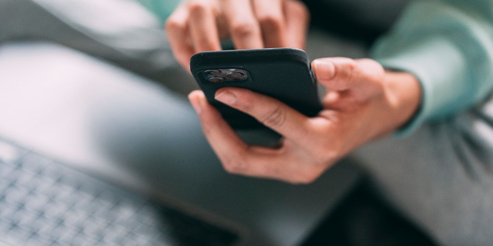 une personne utilise son iphone alors qu'elle est assise avec son ordinateur portable