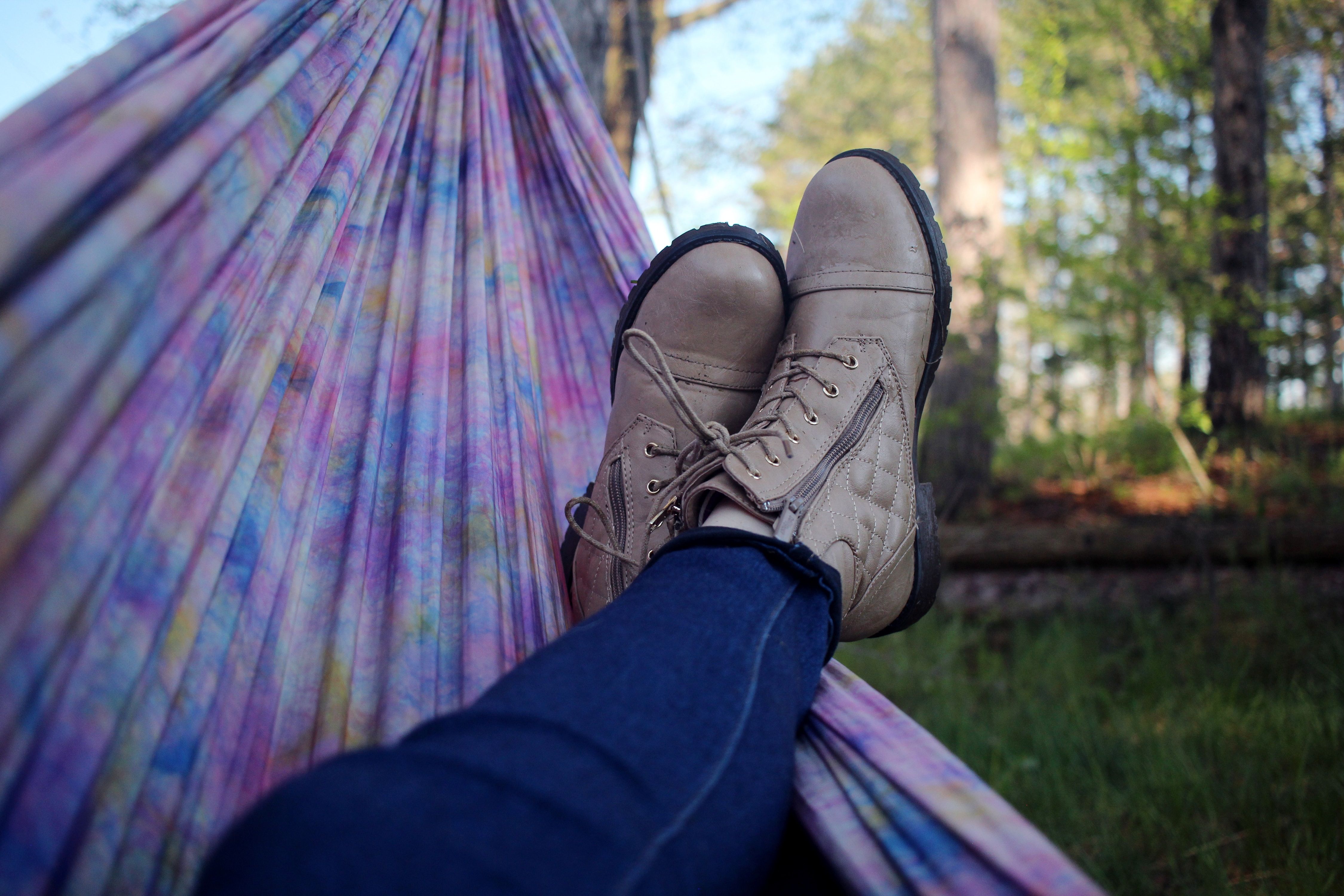 A person relaxing in a hammock outdoors. Only their legs and boots are visible.
