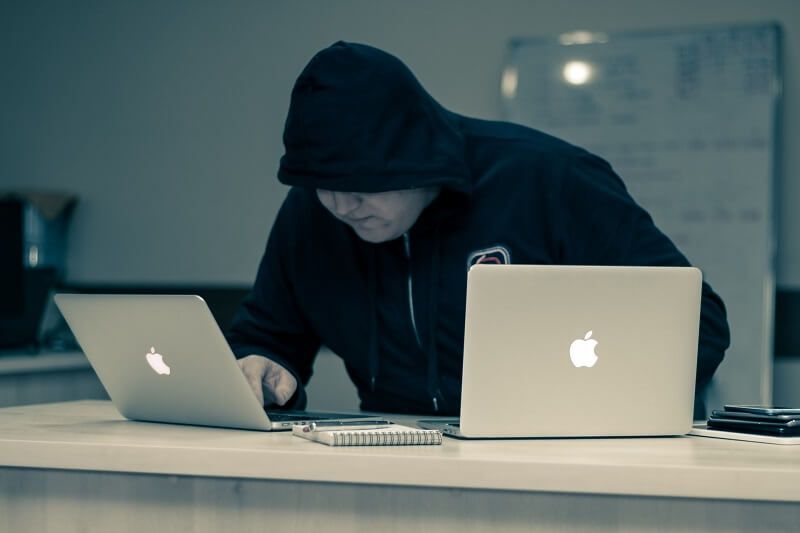 A hoodied hacker with two laptops