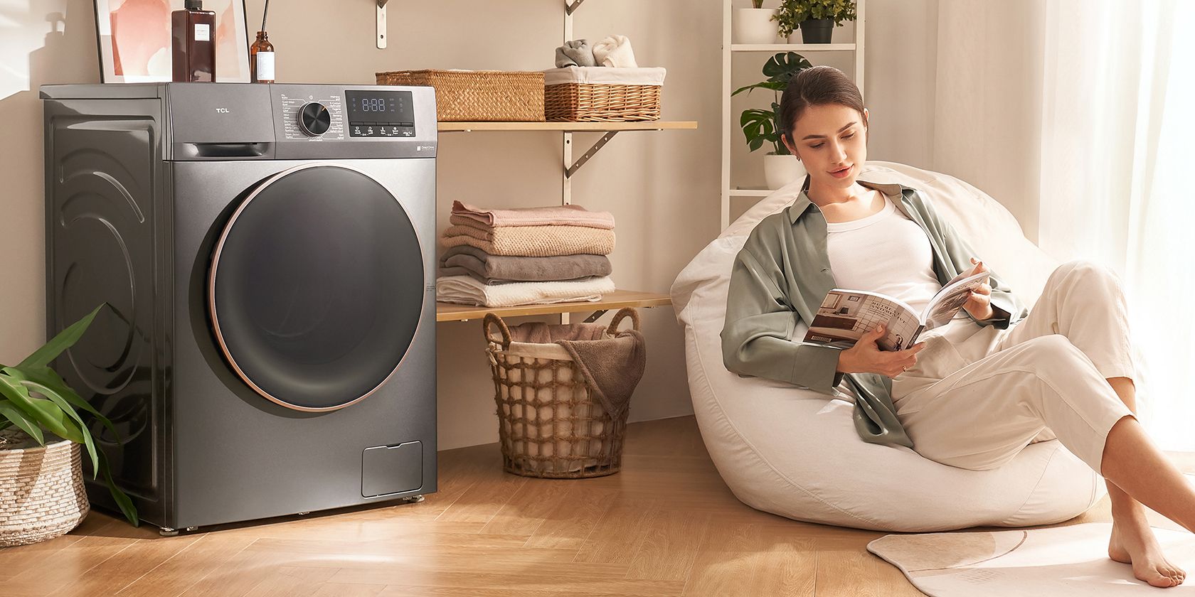 A woman sits on a white pouf reading a magazine beside her TCL Electronics washing machine