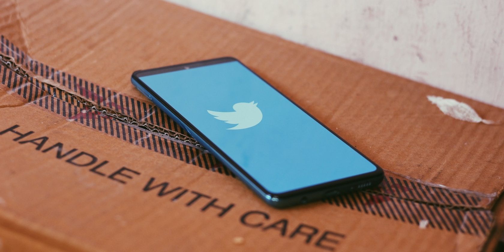 Photo of a phone displaying the Twitter logo ontop of a cardboard box 