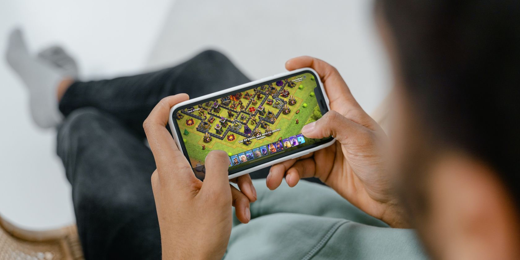 A man sitting down and playing Clash of Clans on an iPhone