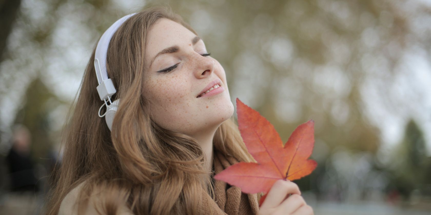 A young woman listens to headphones while holding a leaf outdoors