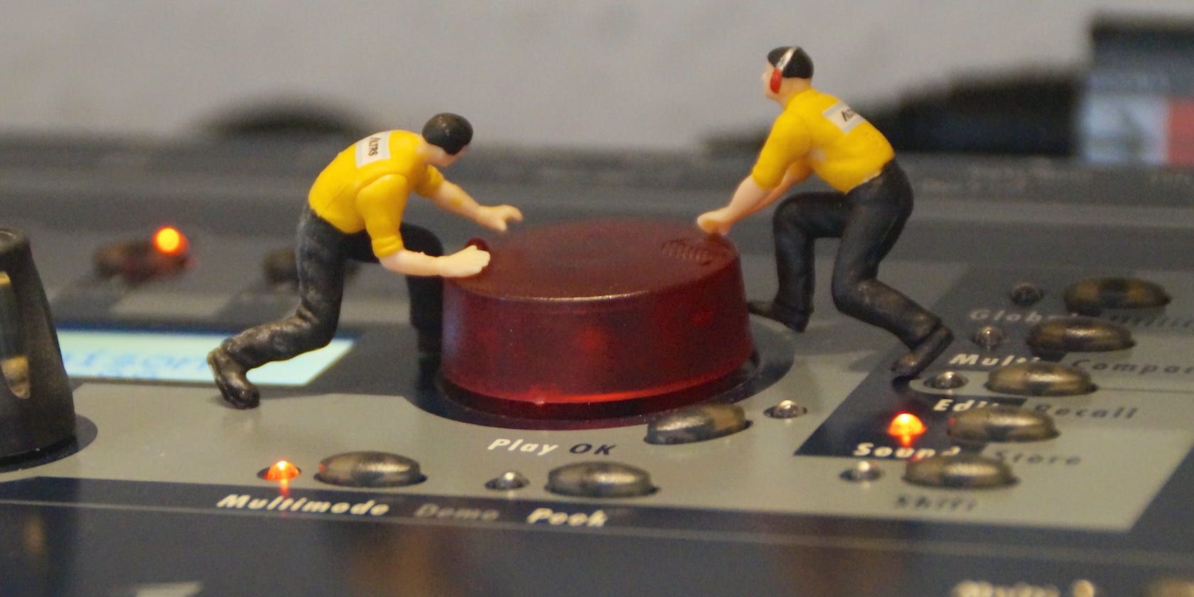 Close-up photo of two minature human figurines turning a knob on a synthesizer