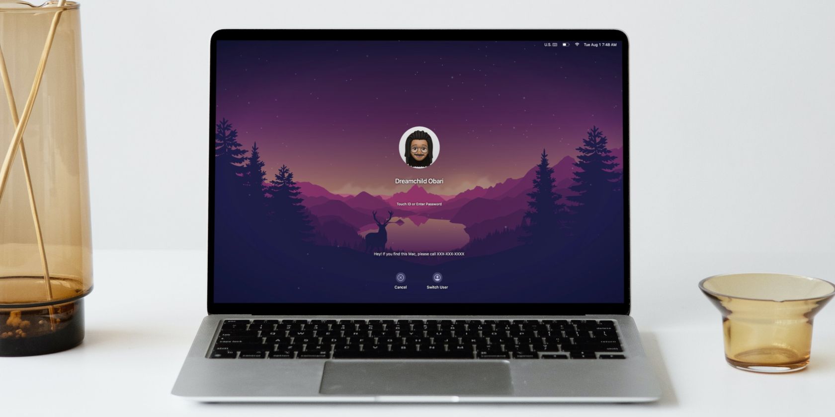 MacBook Air on a white desk displaying a lock screen with a Memoji on screen
