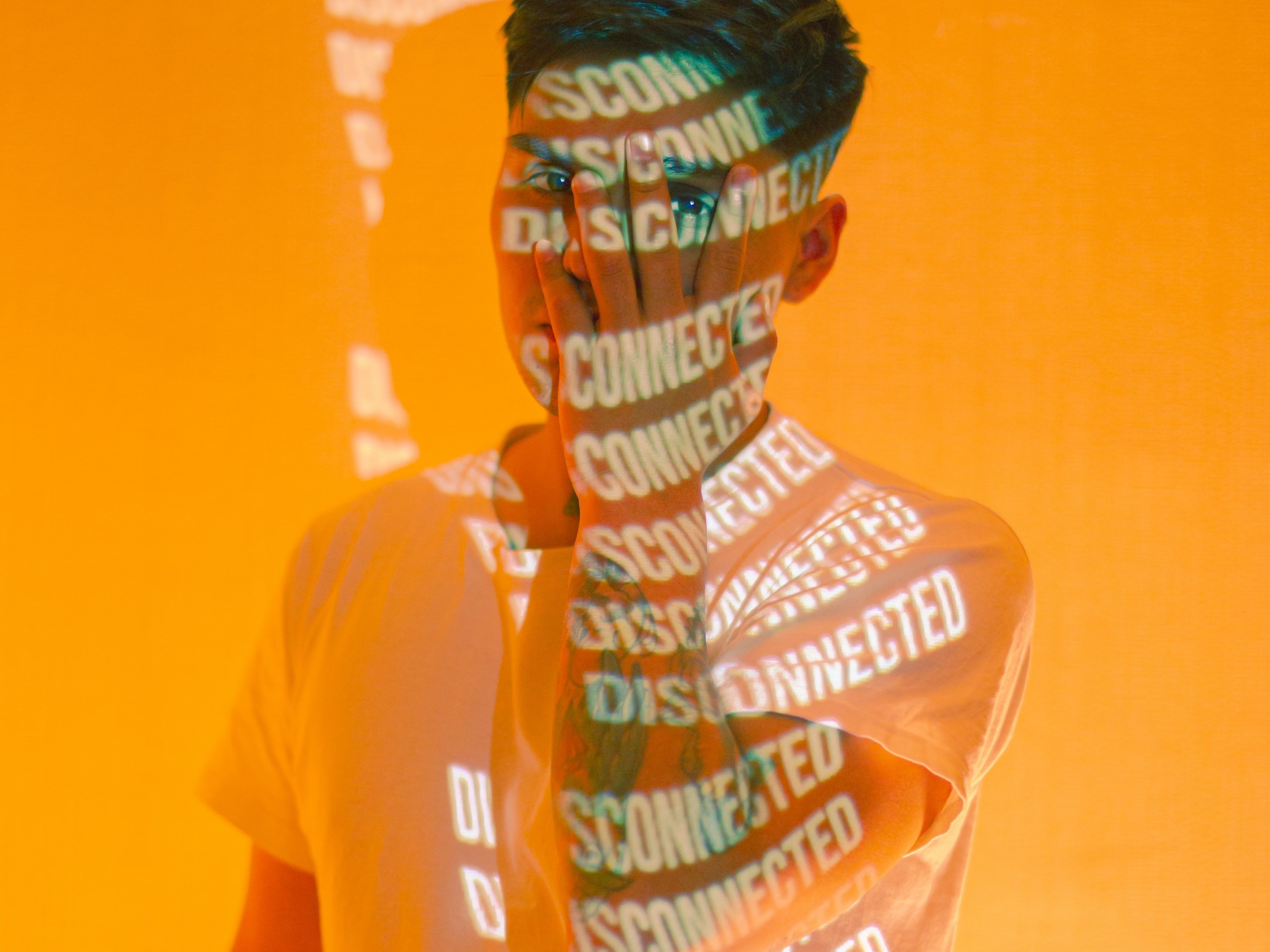 Man With Hand Covering Face Against Yellow Background With the Words Disconnected Projected