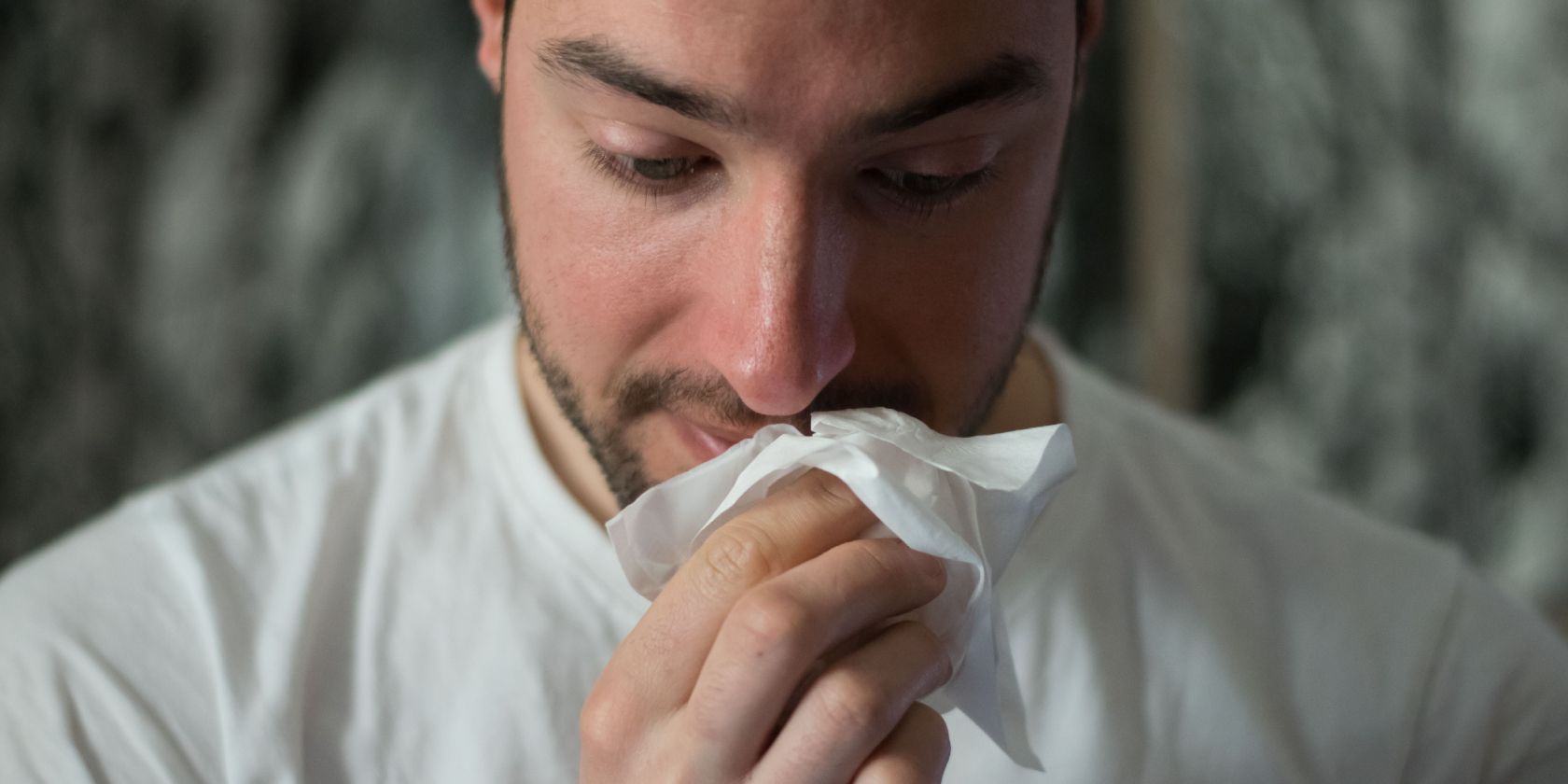 Man holding tissue to his nose as he sneezes