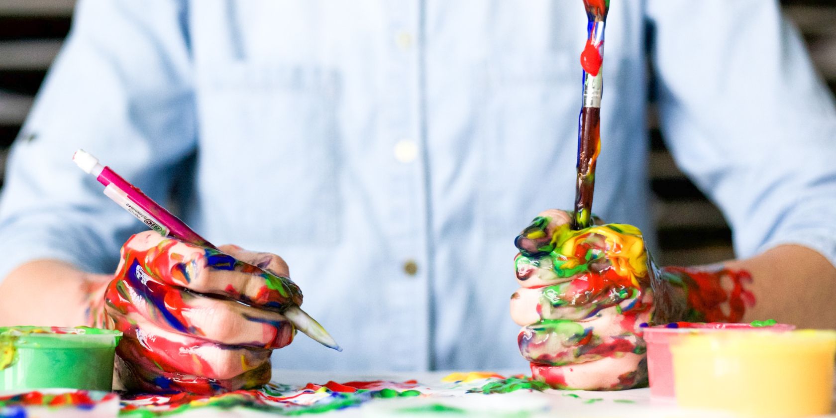 Person holding brushes with hands covered in paint