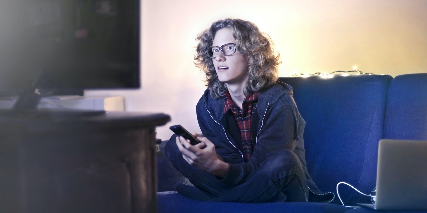 person watching tv with phone and laptop there