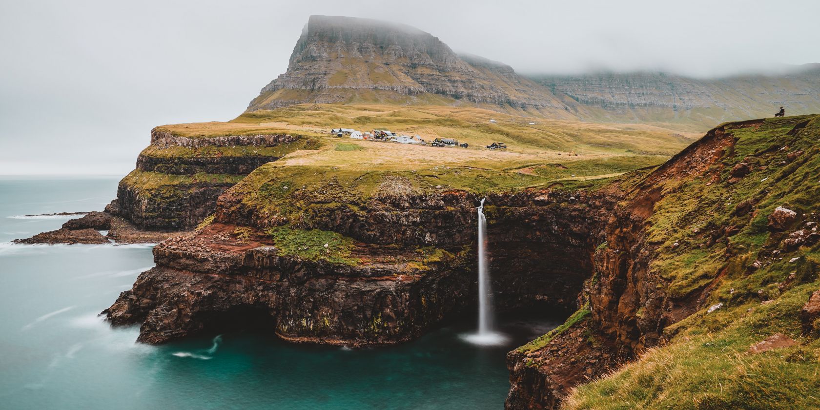 A landscape in the Faroe Islands, featuring a waterfall, cliffs and a mountain