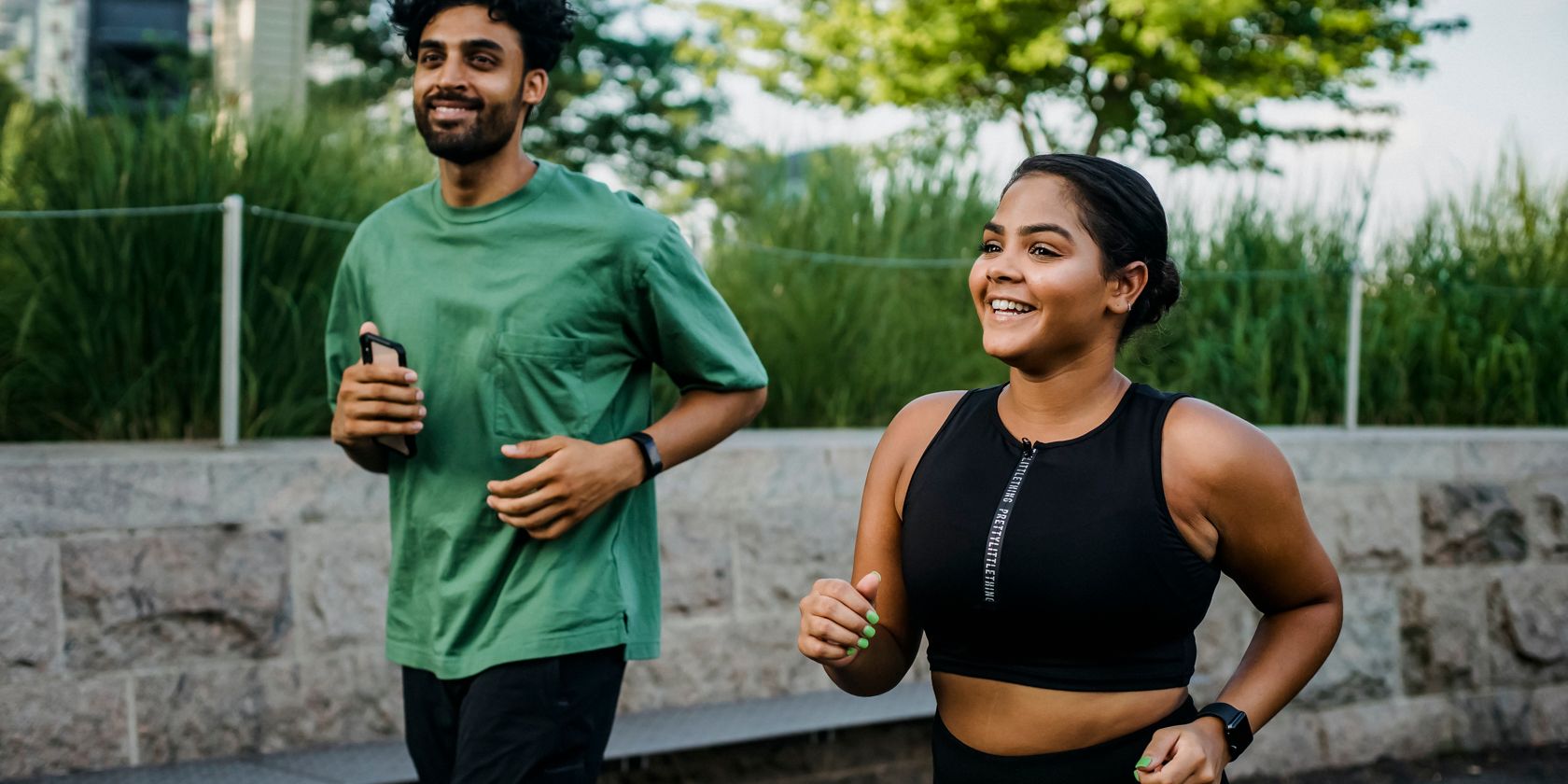 A happy man and woman jogging together wearing smart watches