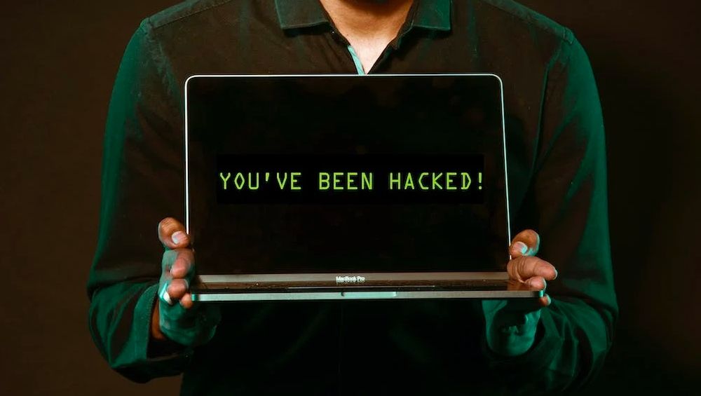 Uma pessoa segurando um laptop com as palavras você foi hackeado na tela