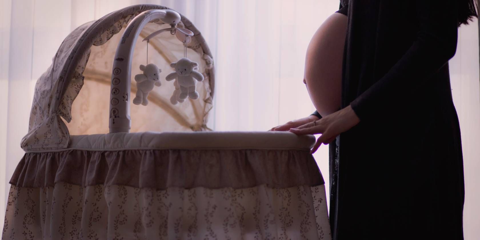 Pregnant woman standing next to a Moses basket