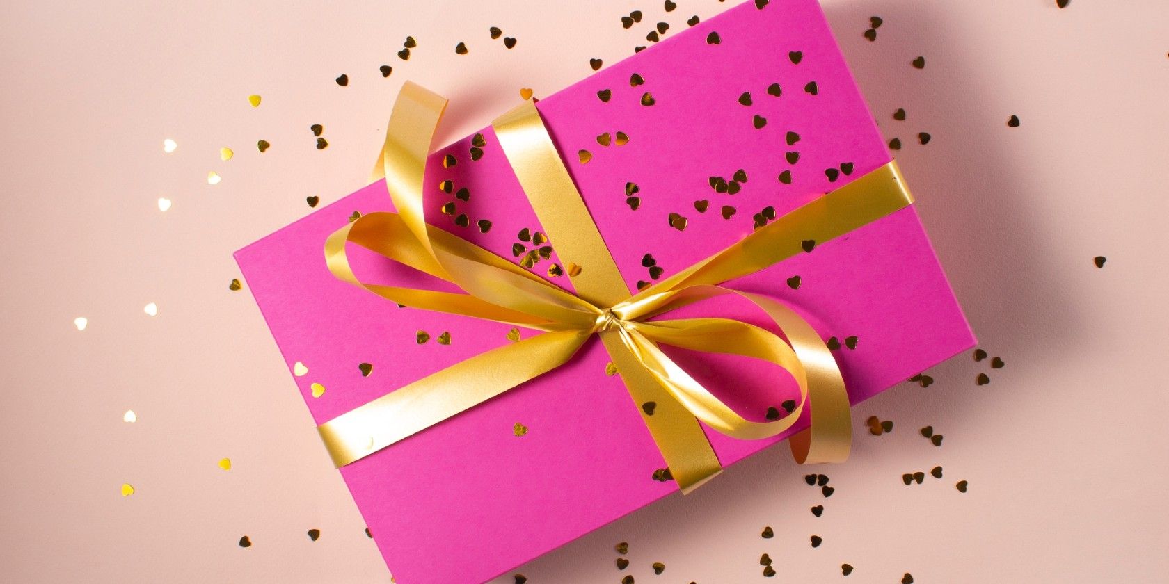 A pink present tied with a golden ribbon sitting on a table.