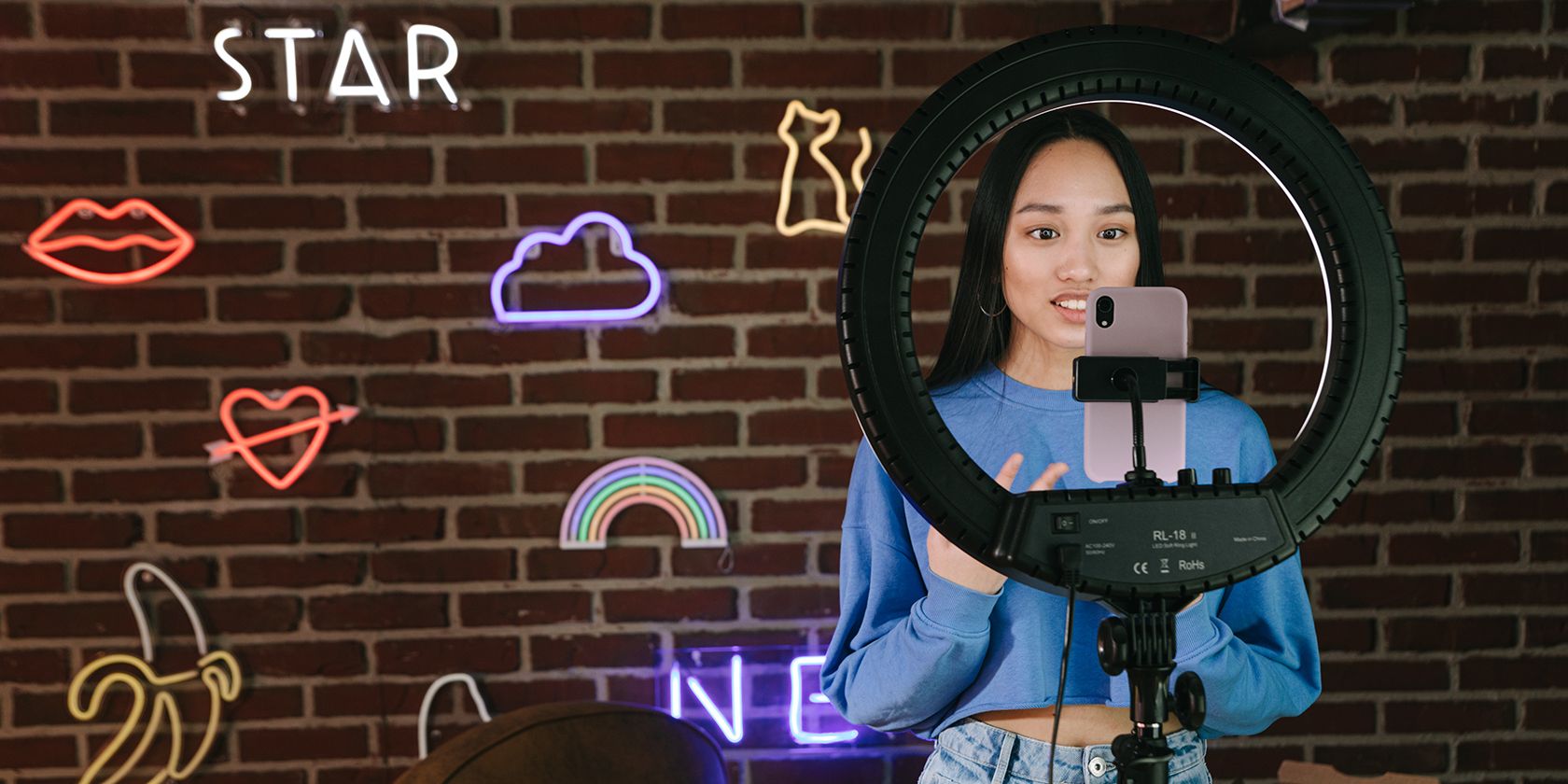 Young woman films video in front of brick wall using phone and ring light