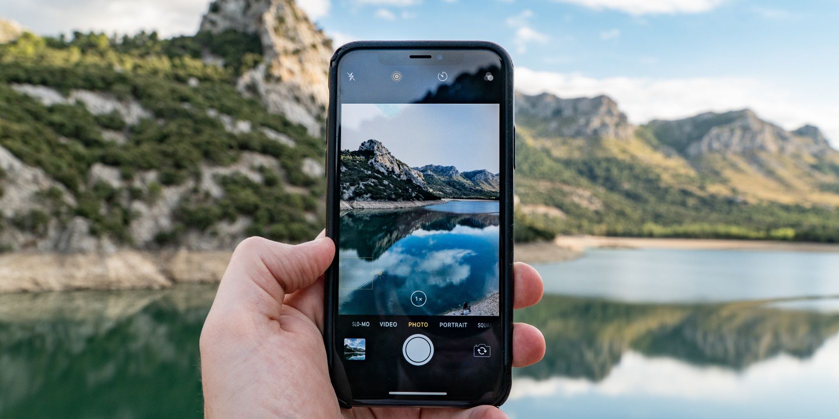 A person holding an iPhone to take a picture of a lake