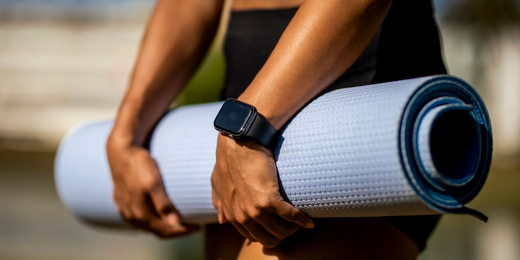 A person in black shorts wearing an Apple Watch holds a rolled up yoga mat