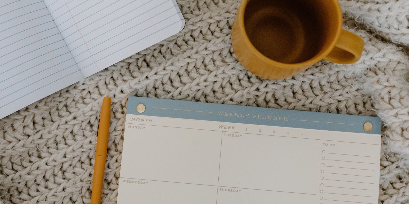 weekly planner, notebook, and coffee on a table