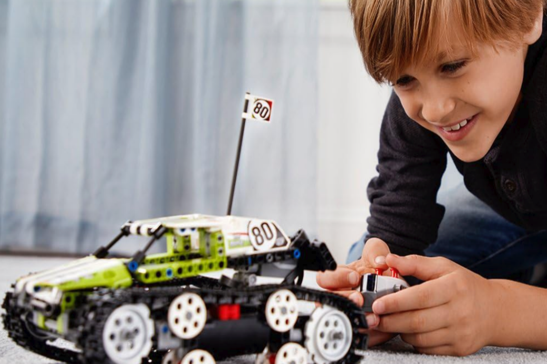 A young boy playing with LEGO Technic RC Tracked Racer